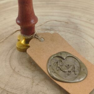 Close-up of a wooden stamp with a gold base resting on a kraft tag tied with twine, on a wooden surface.